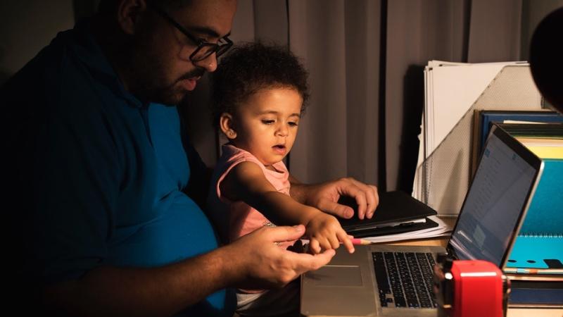 A father is sitting at his desk with laptop open while holding his baby on his lap
