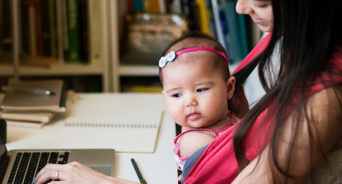 Photo of mother on laptop with baby on her lap